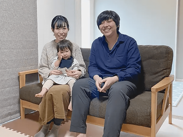 小さい子と両親の家族3人が笑顔でソファに座っている様子